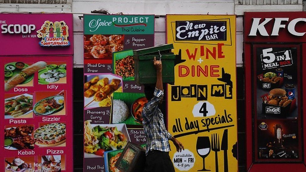 An Indian vendor walks past promotional posters for restaurants in Kolkata