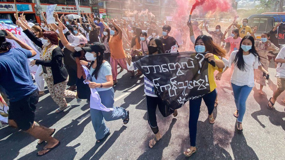 Женщины с транспарантами, сигнальными ракетами и пожарными шашками маршируют во время демонстрации против военного переворота в Янгоне в июле 2021 года