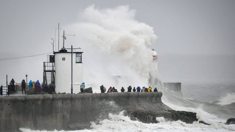 People watch waves and rough seas pound against the harbour wall at Porthcawl
