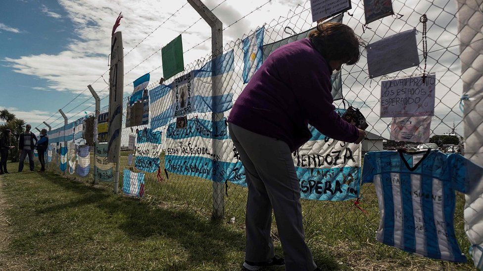A woman hanging a message of support on an Argentine flag on a fence