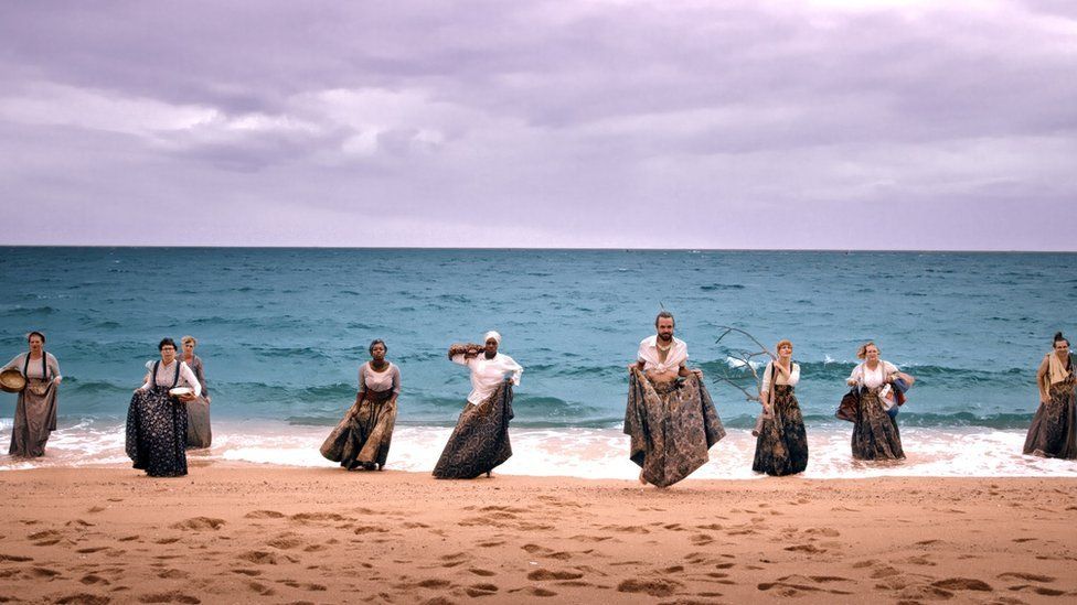 People on a beach performing I am Kevin by Wildworks