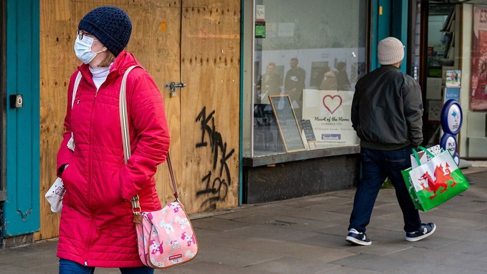 A woman wearing a face mask walks past a closed shop on February 2, 2022, in Newport, Wales.