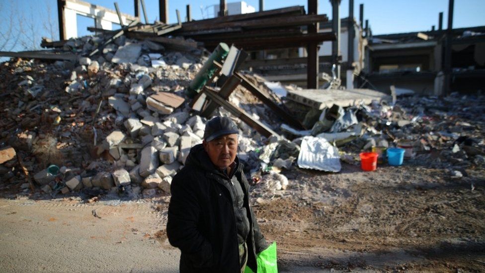 A local resident walks near the debris of a building demolished by local officials during a citywide fire safety inspection in November 2017, in Beijing