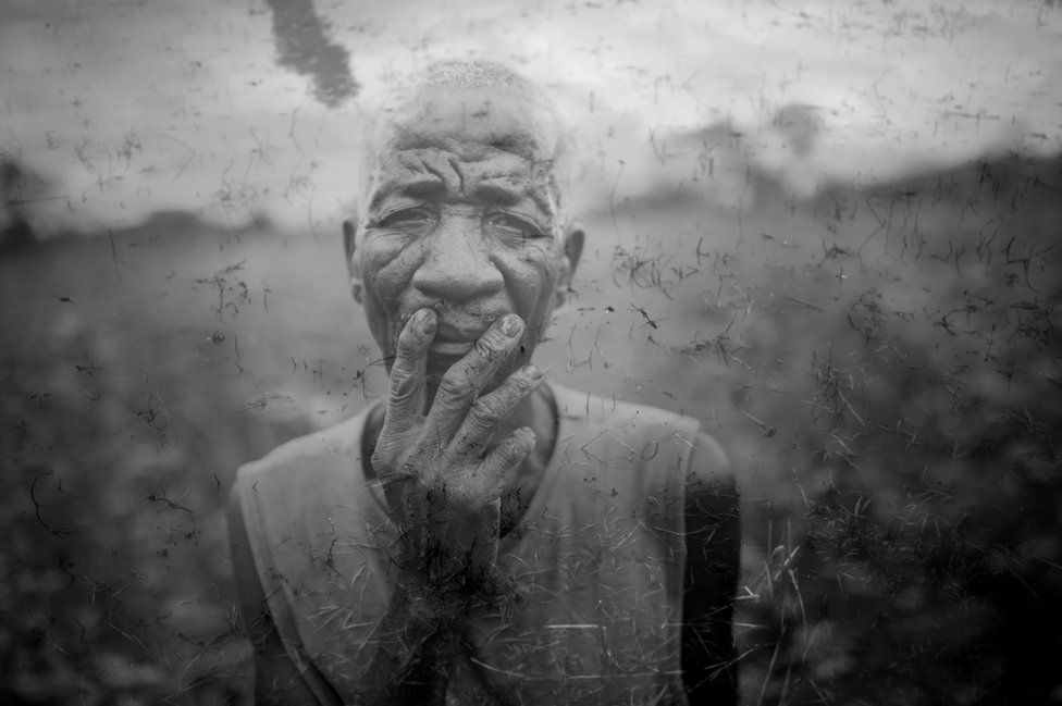 An elderly farmer stands in his field, overlaid onto an image of a puddle of murky water