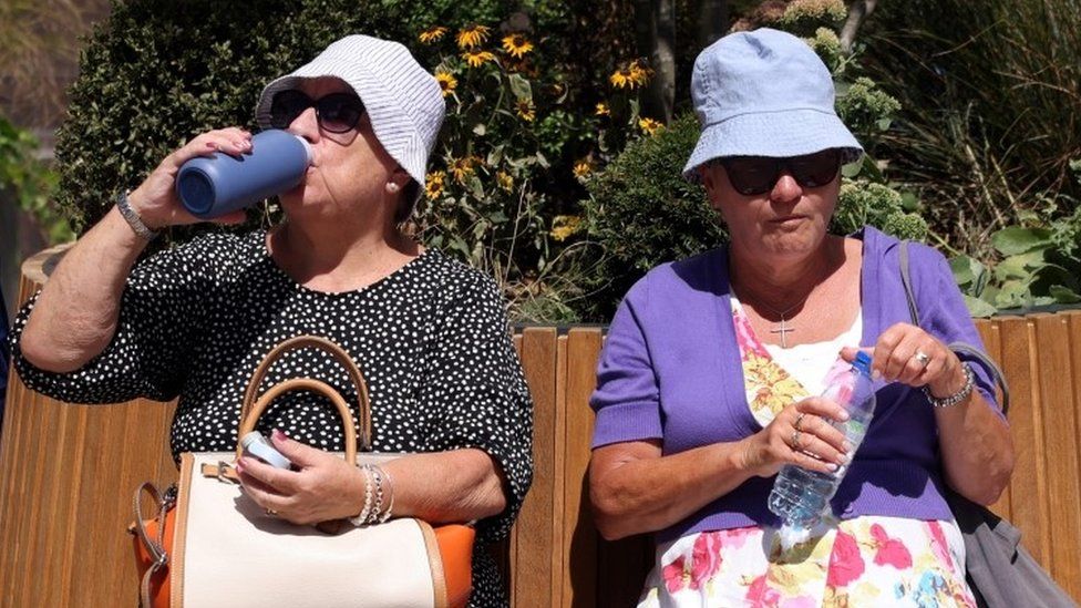 Two women drink water while sat outside