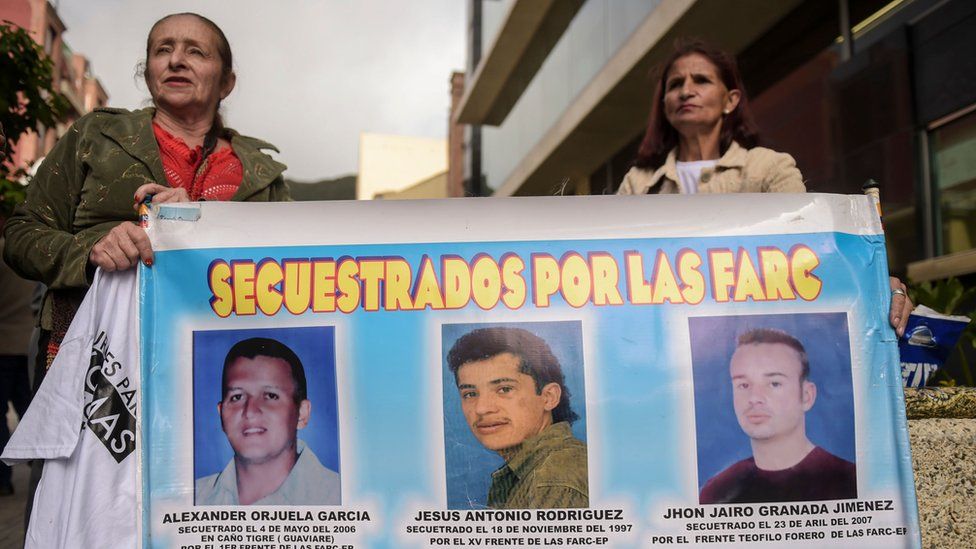 Women hold a banner with the portraits of three men kidnapped by the FARC guerrilla, during a protest outside at the Special Jurisdiction for Peace (JEP) headquarters in Bogota on July 13, 2018.