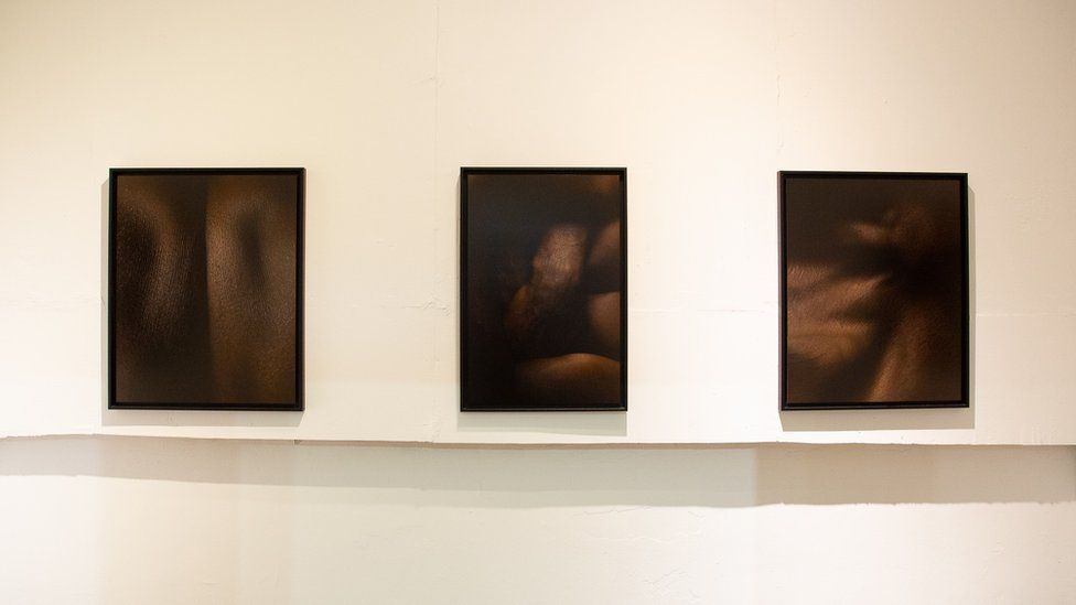 Photographs of black bodies by Rwandan artist Gilles Dusabe hang.