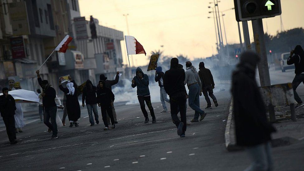 Bahraini protestors run for cover from tear gas fired by police during clashes at a protest in Sitra on 29 January 2016