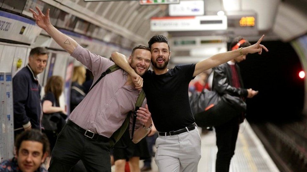 Passengers pose for a photograph as they wait for the Night Tube train service