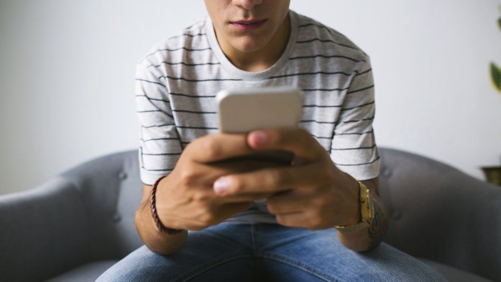 A teenage boy head out of frame using a mobile phone (stock image)