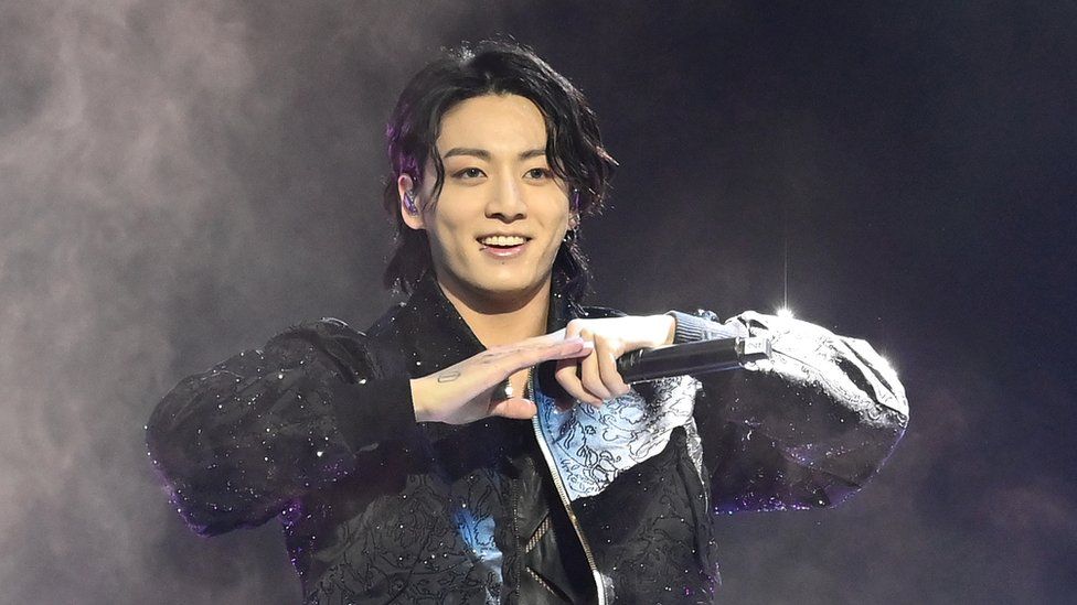 Jung Kook is connected  stage, wearing a leather overgarment   with sparkly jewels dotted astir   it. He's holding a microphone, his hands unneurotic  astatine  the fingertips astatine  thorax  height. He's smiling, arsenic  if he's conscionable  finished a performance, and his ear-length acheronian  hairsbreadth  looks somewhat  matted arsenic  if from exerting himself. There's a faint wisp of fume  oregon  adust  crystal  down  him connected  the different    achromatic  background.