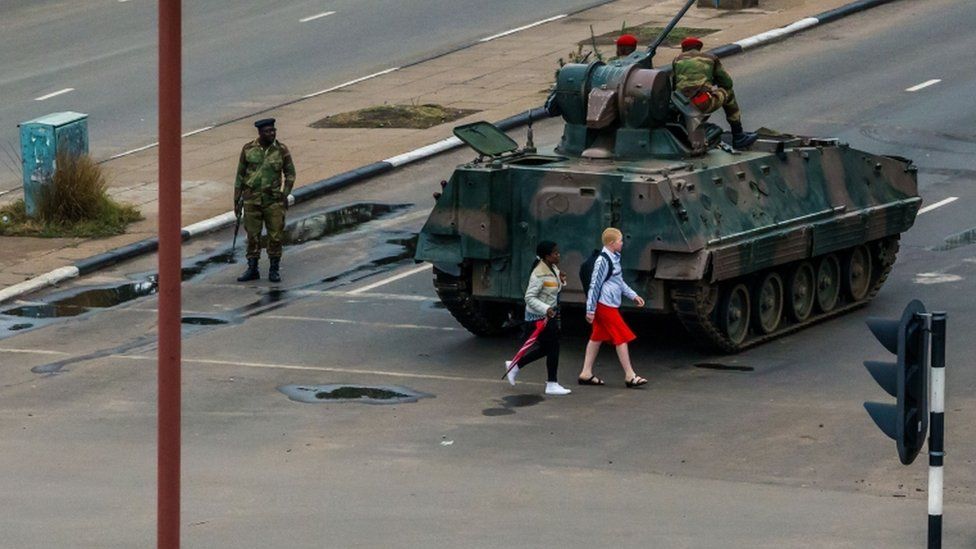 Young women walk past an armoured personnel carrier in Harare, 15 November
