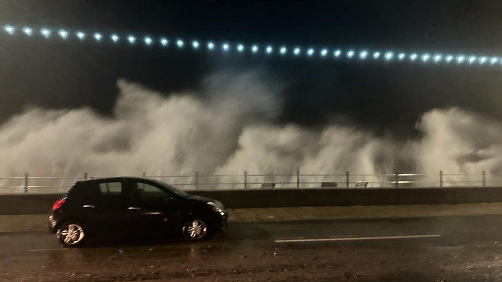 Waves crash into Penzance promenade in Cornwall as a car drives by