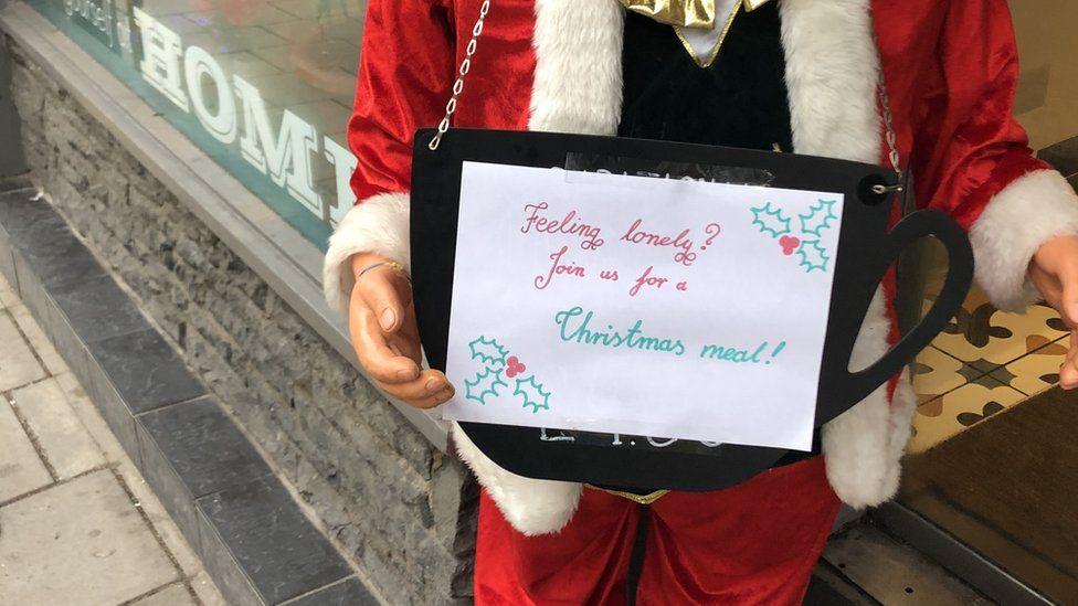 Santa holding up a sign inviting lonely people in for food