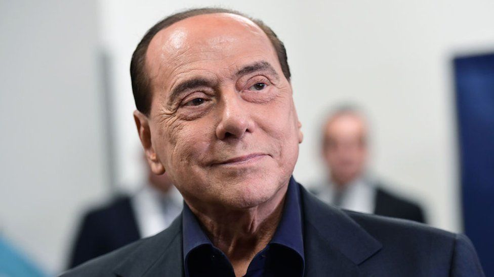 Silvio Berlusconi smirks, looking confident, at a polling station after casting his vote