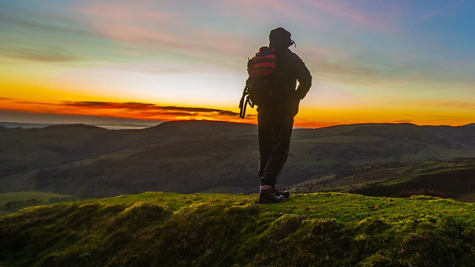 A walker looks out at the break of dawn across the Clwydian Range