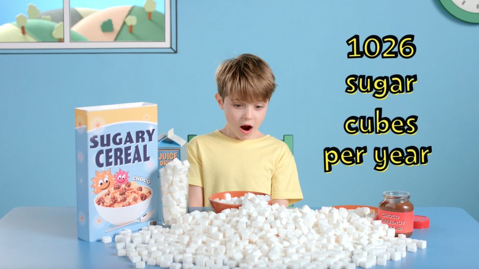 A boy surrounded by sugar cubes at breakfast and a packet of sugary breakfast cereal