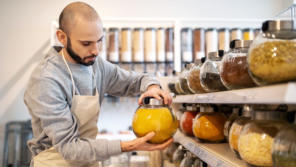 Stock image of a shop owner holding a jar of spices