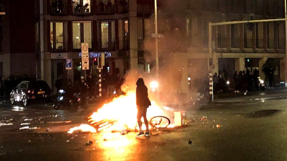 Silhouette of person standing by bike on fire at Dutch protest