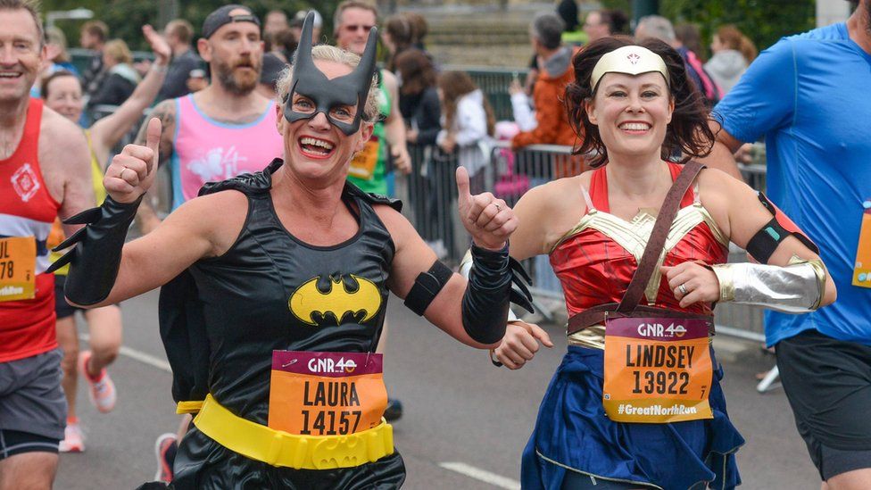 A female runner in a Batwoman costume gives a thumbs-up