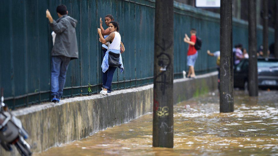 People climb along a fence to pass a flooded area