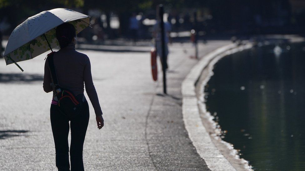 A woman shading from the heat while walking with an umbrella