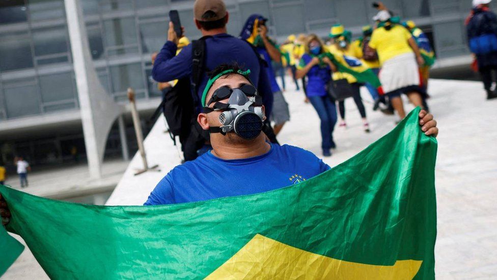 Man with gas mask and Brazilian flag outside Congress building