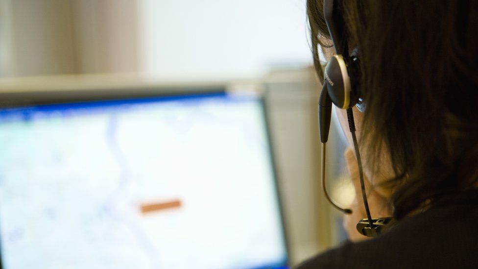 An exigency  dispatcher pictured from behind. Her microphone and machine  surface  are visible.