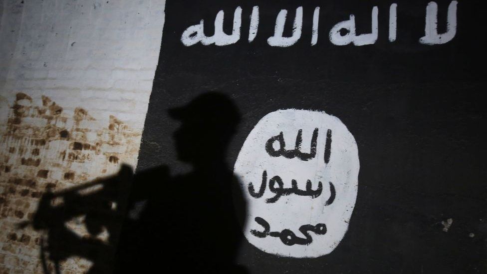 A member of the Iraqi forces walks past a mural bearing the logo of the Islamic State