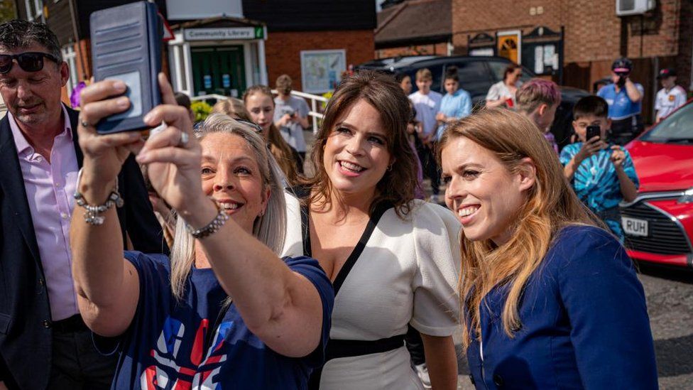 Princesses Beatrice and Eugenie pose for a selfie with a well-wisher while attending a street party on Sunday