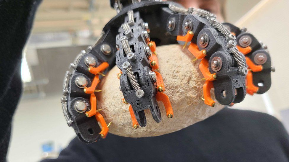 A man holds a robot claw gripping a rock