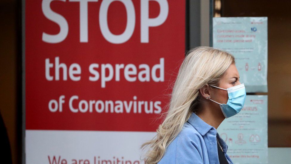 A woman wearing a face mask walks past a coronavirus sign in Glasgow
