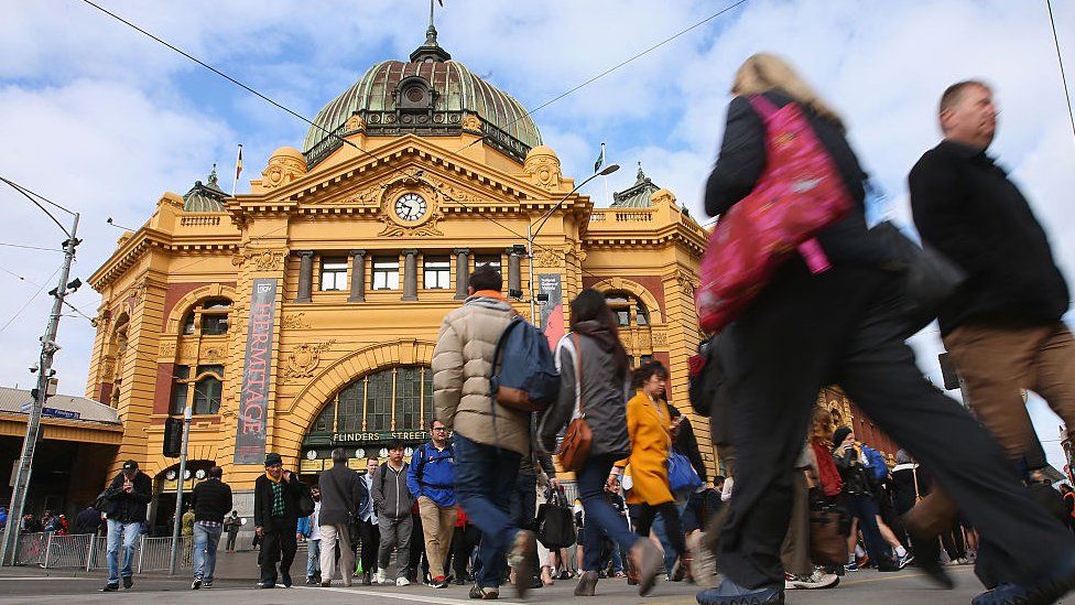 Pedestrians cross the road in front of Flinders Street Station