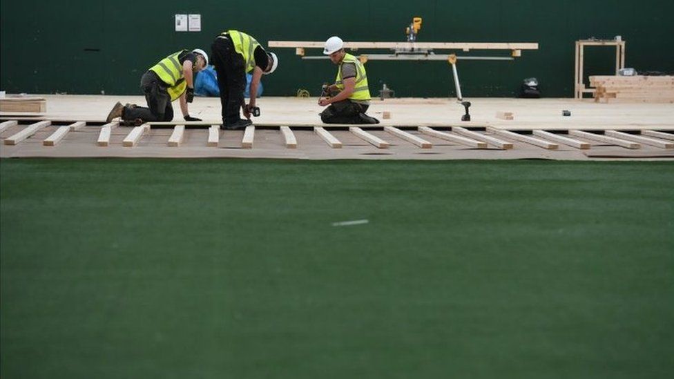 Workers lay flooring during the construction of a field hospital at Llandarcy sports academy in Neath