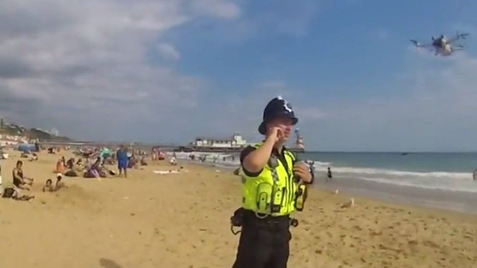 A police officer on Bournemouth beach and a drone coming down to land