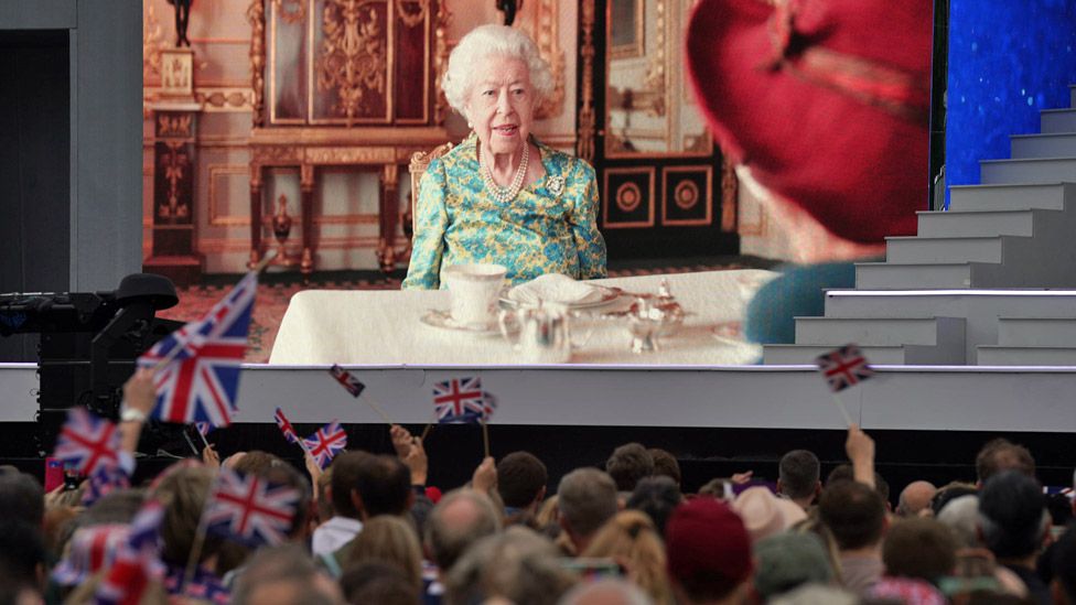 The Queen and Paddington Bear on a big screen, with people waving union flags in the foreground
