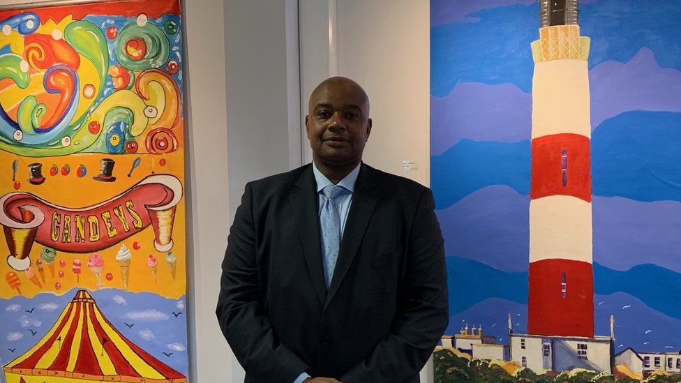 Deputy Prison Governor Leroy Bonnick standing in front of two paintings