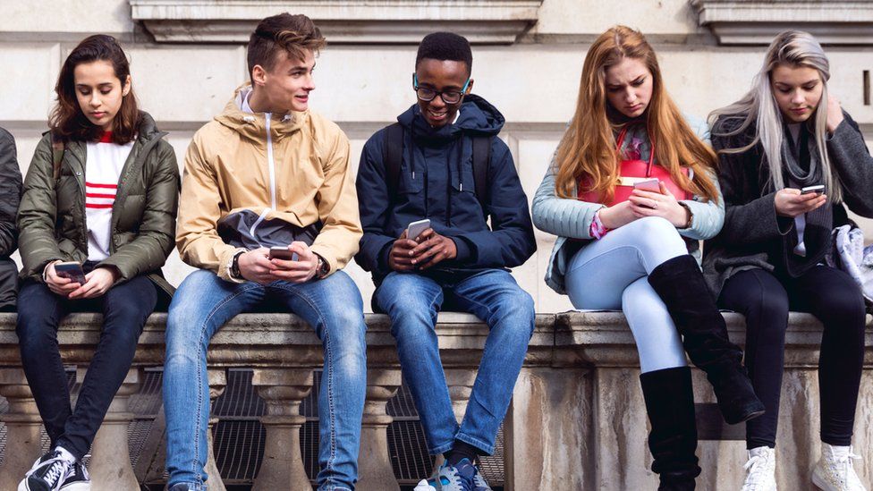 Teenage boys and girls sitting together using their phones