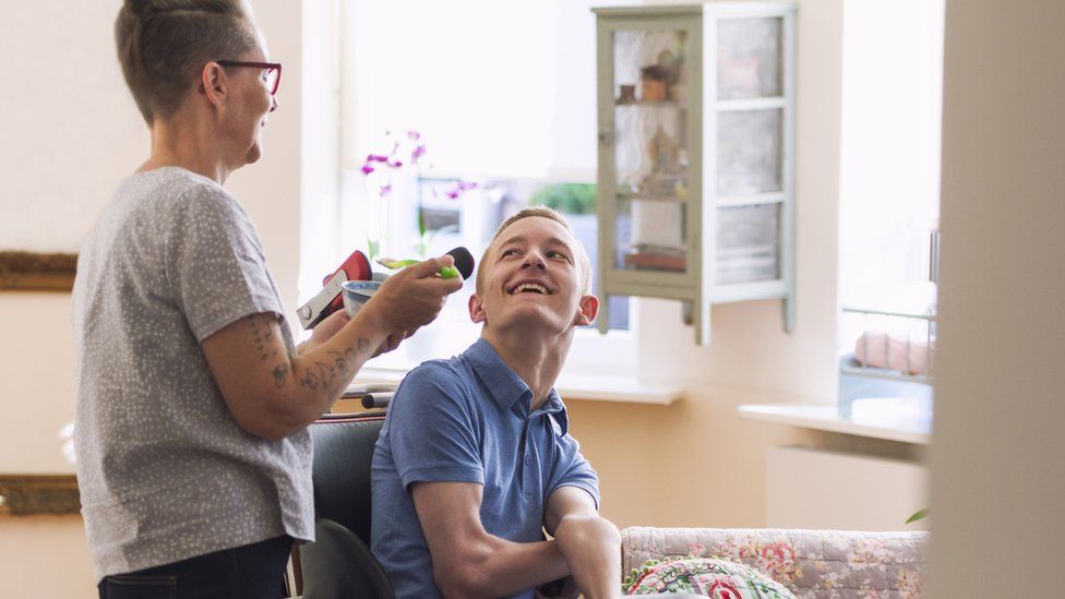 A young man with Cerebral Palsy is helped by a carer