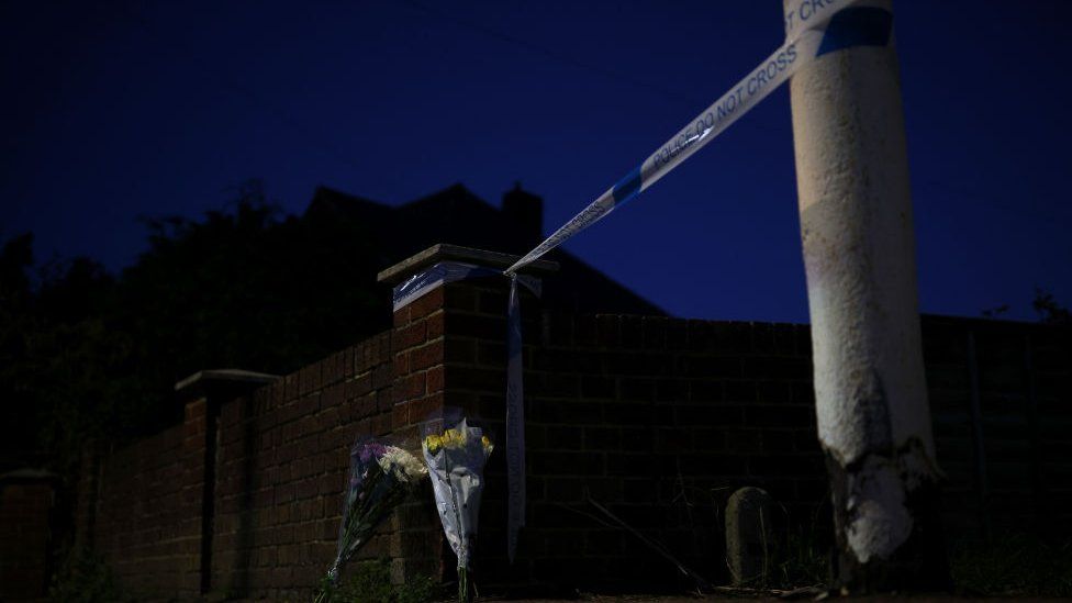 Police tape with bunches of flowers laying in front of it