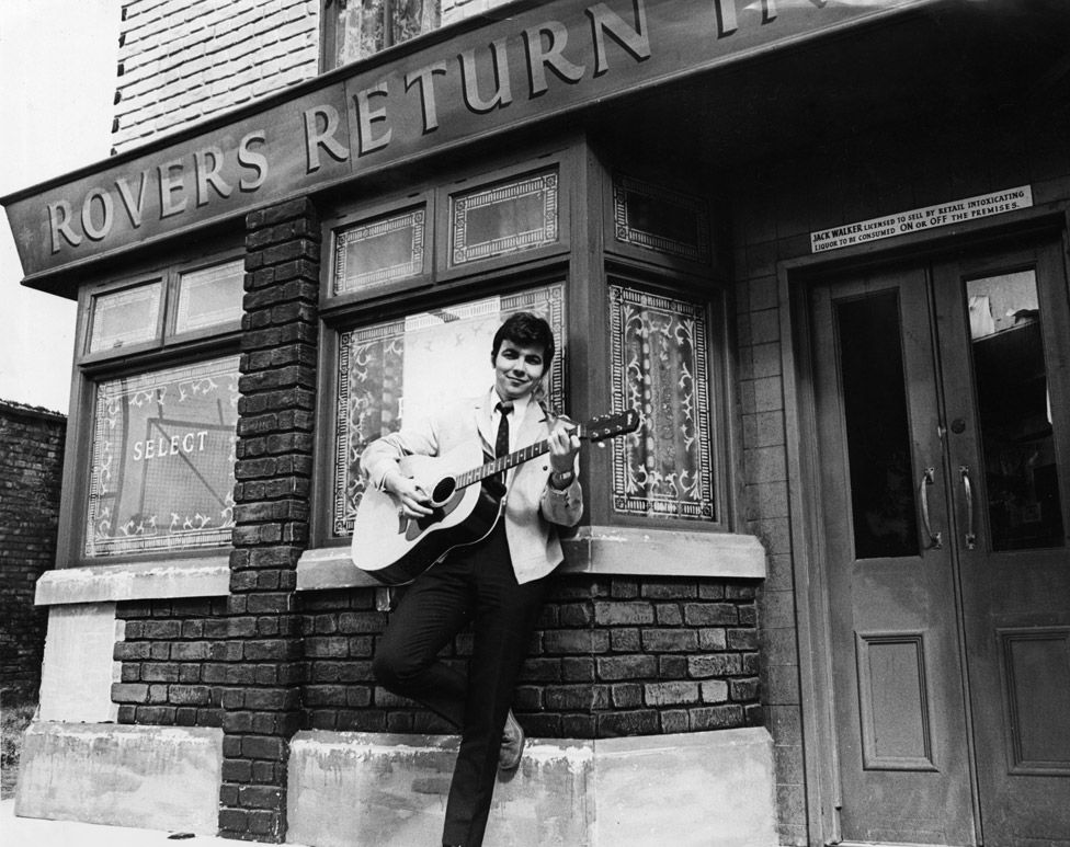 Actor Bill Kenwright who plays Gordon Clegg in the television soap opera Coronation Street, poses in the famous street with his guitar shortly before the release of his new record which he will sing on the programme, 23rd July 1968
