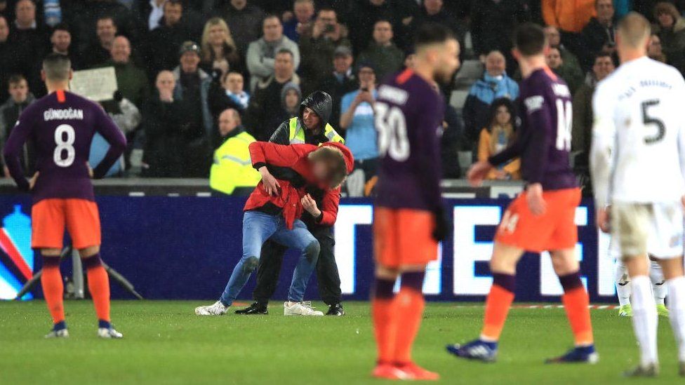 A fan is stopped on the pitch by a steward during one of the two pitch invasions