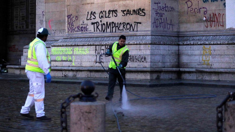A worker hoses the ground by the Arc de Triomphe, in front of graffiti reading: "The yellow vests will triumph"