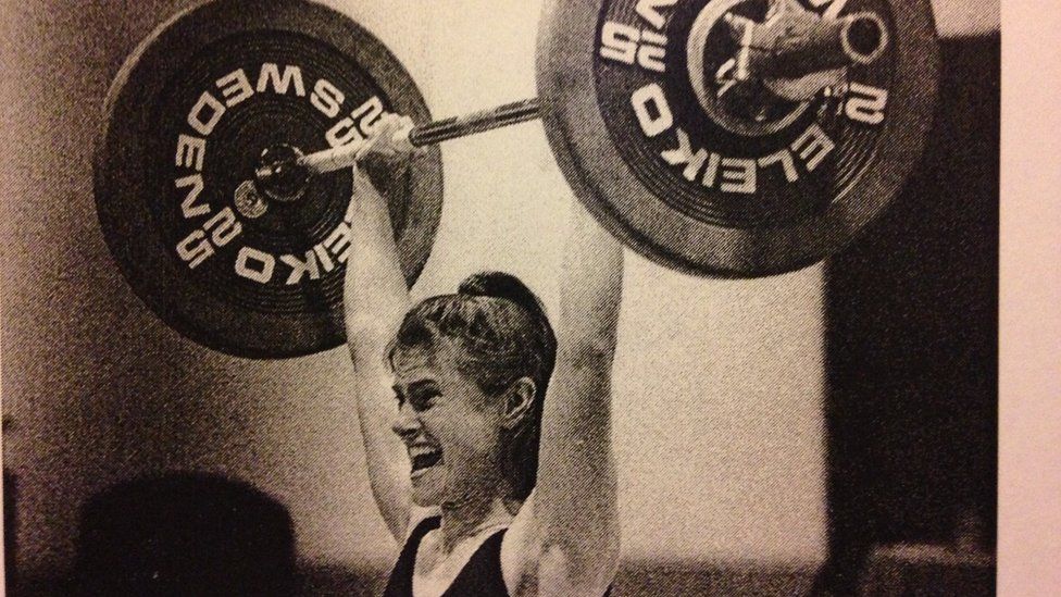 A black and white photo of Trish Tenn lifting a barbell above her hed