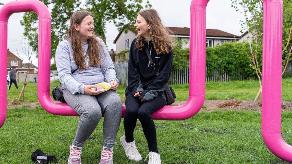 Two girls sitting on a pink play park facility