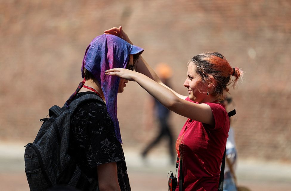 Женщина надевает на мужчину мокрый шарф, чтобы защитить его от солнца в Болонье, Италия || |