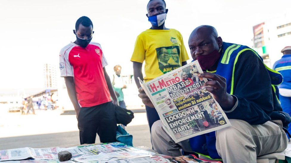 People read newspaper headlines over the shoulder of a vendor in Harare on January 5, 2021