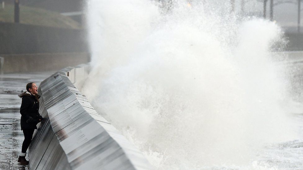 A girl looking as high waves crash into a barrier in a storm