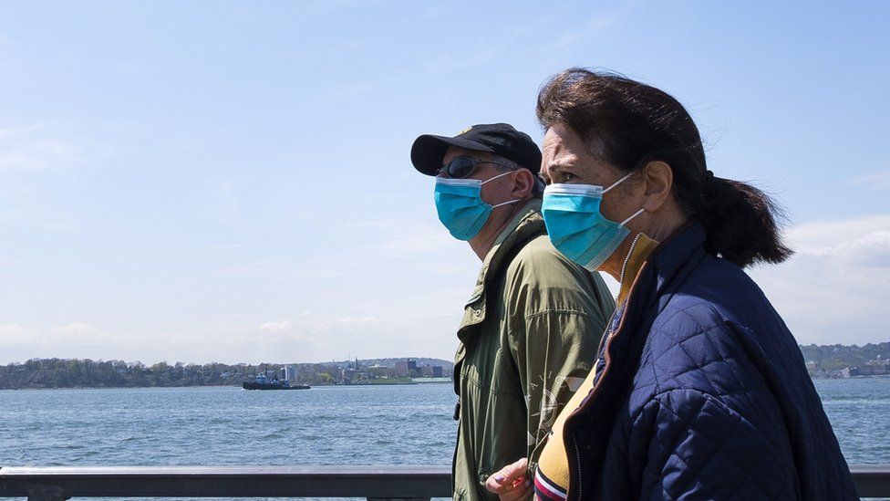 People in masks walk along New York Harbor in New Yor