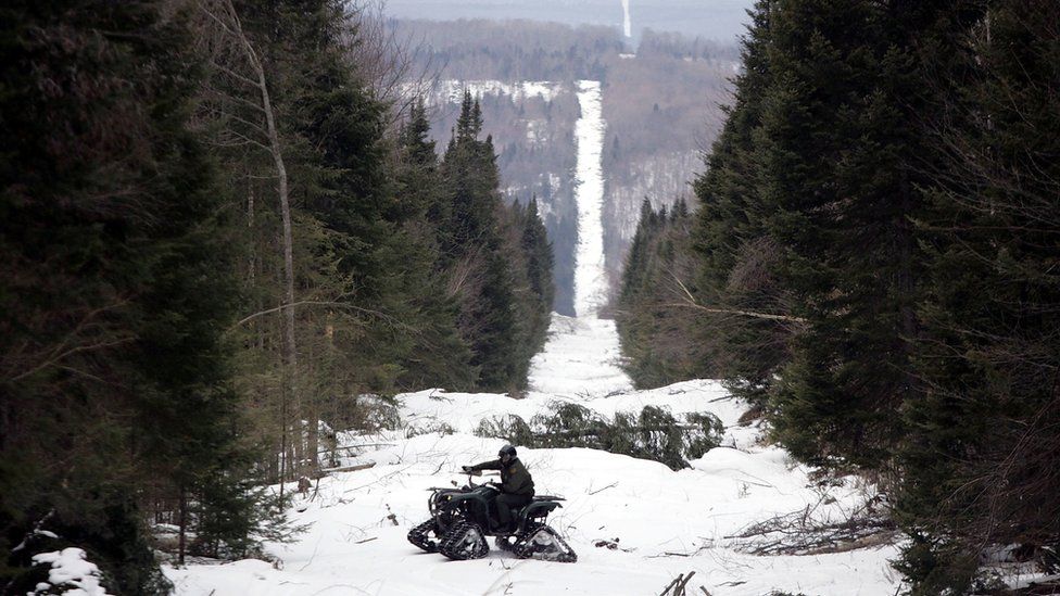U.S. Border Patrol Agent Andrew Mayer rides a ATV as he looks for signs of illegal entry along the boundary marker cut into the forest marking the line between Canadian territory on the right and the United States March 23, 2006 near Beecher Falls, Vermont.